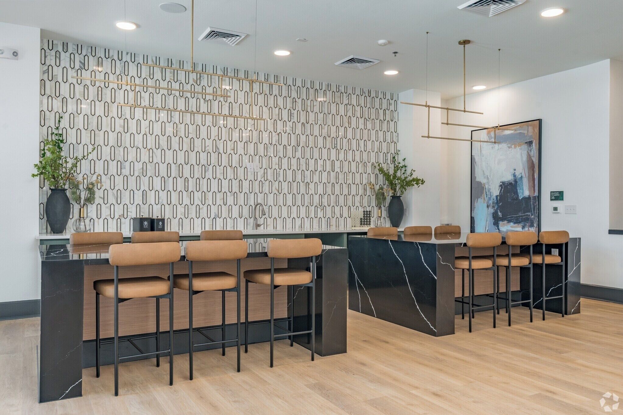 Un espace d’accueil moderne avec un mur orné d’un motif décoratif, des tabourets de bar et un grand tableau abstrait.