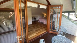 A room with wooden flooring, a bed with a pink bedspread, a chair, and a table with a metal design. - A Little Piece of Paradise – Cottage Point Waterfront Retreat (Cottage Point)