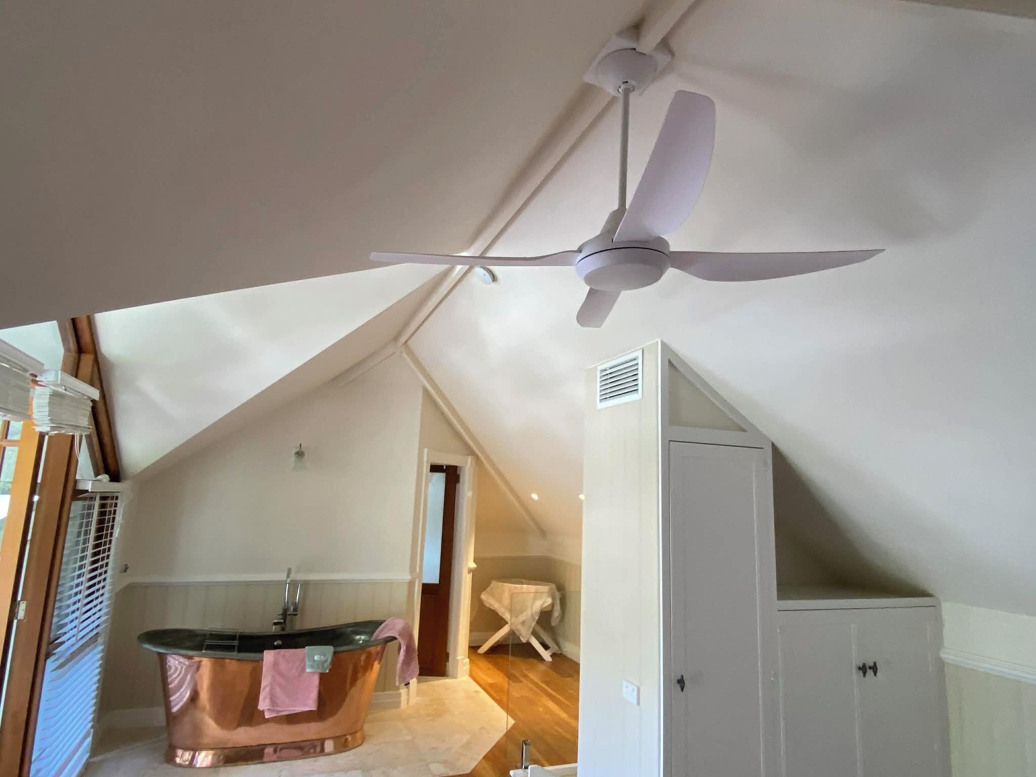 Una habitación con ventilador de techo, bañera y un armario blanco.