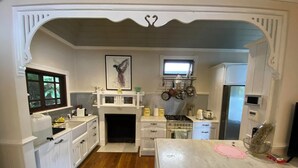 A kitchen with white cabinetry, a gas stove, a microwave, and a window with a view of greenery. - A Little Piece of Paradise – Cottage Point Waterfront Retreat (Cottage Point)