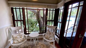 A room with a bay window, two white wicker chairs, a small round table, and a patterned rug. - A Little Piece of Paradise – Cottage Point Waterfront Retreat (Cottage Point)
