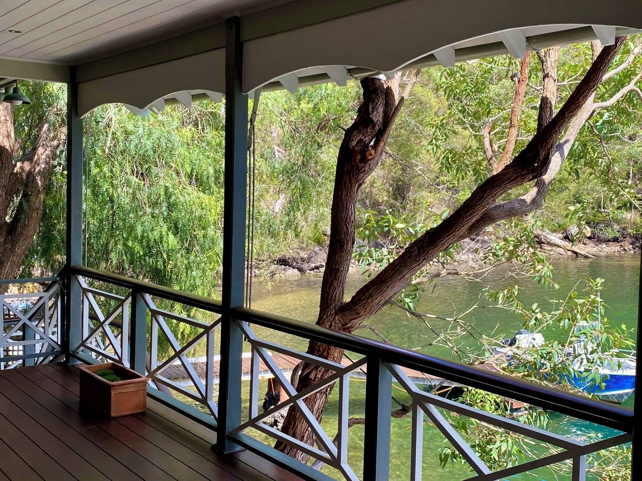 A covered outdoor area with a view of a river, a railing, and a potted plant.