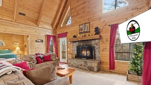 Interior acogedor de una cabaña de madera con chimenea de piedra, paredes de madera y un árbol de Navidad.