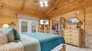 Un dormitorio de cabaña de madera con una cama, cómoda y televisor en una pared de madera.
