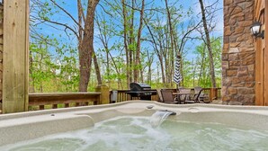 Un jacuzzi con cubierta de madera y pared de piedra, rodeado de árboles.