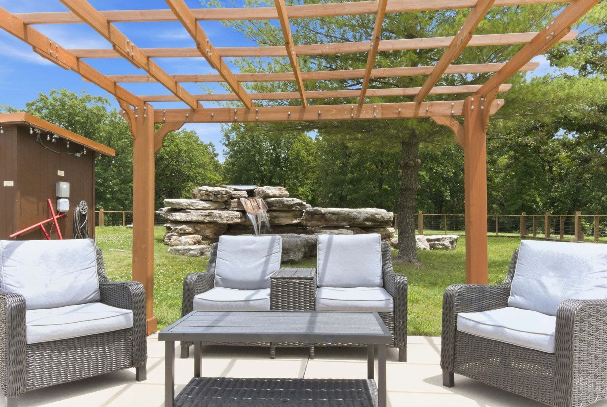 Un patio al aire libre con mobiliario de mimbre, una pérgola y una fuente de piedra con cascada.