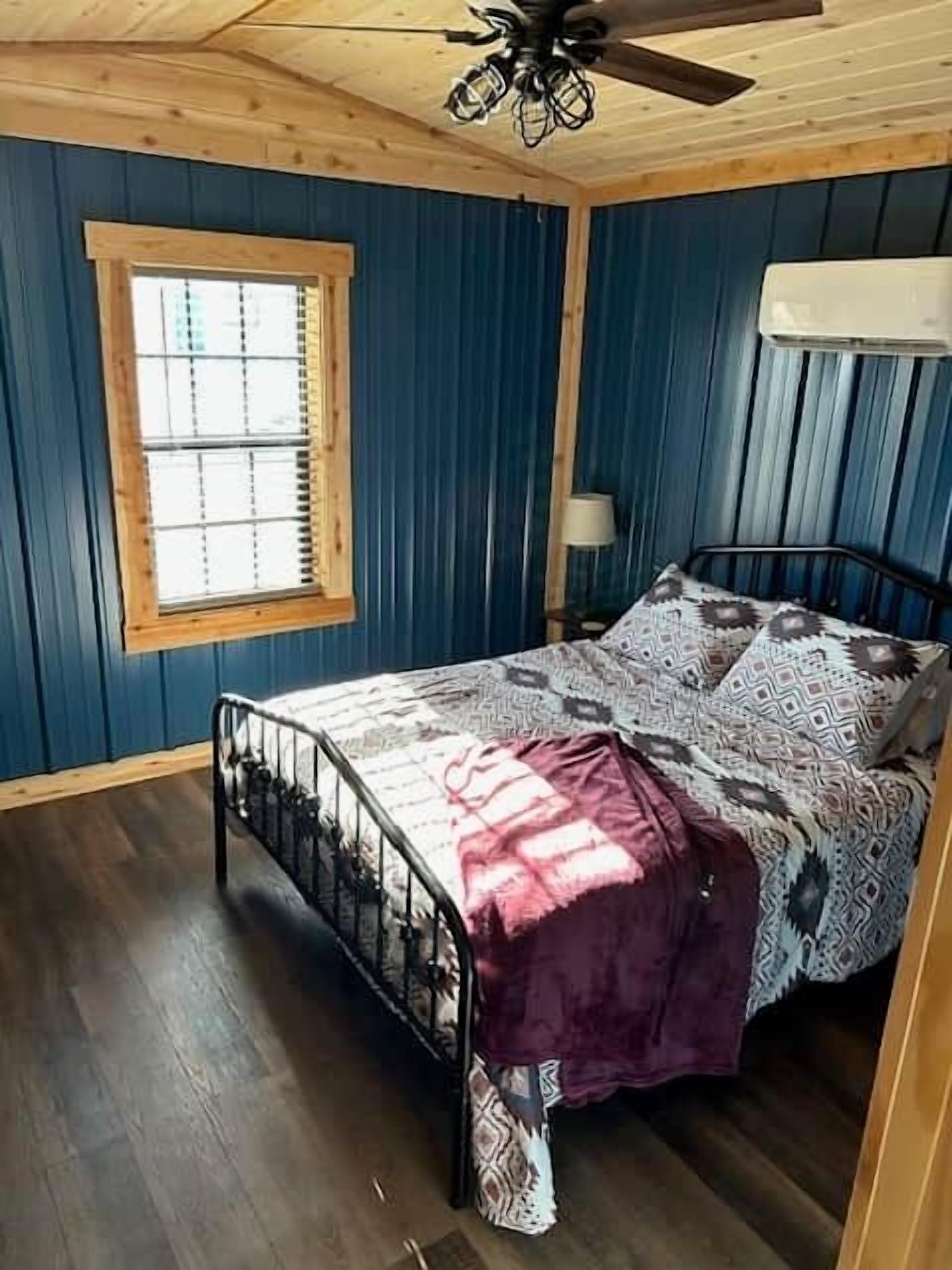 Une chambre à coucher comprenant un lit, une fenêtre avec des stores, un ventilateur de plafond et un climatiseur fixé au mur.