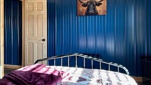A bedroom with a bed, a door, and a blue wall with a bull head painting.