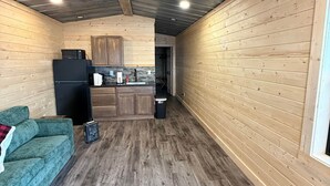 A cozy cabin interior with a wooden floor, a green sofa, a kitchen area with wooden cabinets, and a ceiling fan. - The Cabin in Tribune (Tribune)