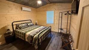 A wooden cabin bedroom with a bed, a hanging clothes rack, a window with blinds, and a ceiling fan. - The Cabin in Tribune (Tribune)