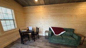 A cozy room with a wooden interior, a green sofa with a red and white blanket, a small table with a menu, and a window with blinds. - The Cabin in Tribune (Tribune)