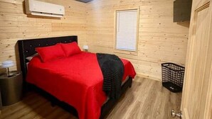 A wooden cabin bedroom with a bed, a ceiling fan, an air conditioning unit, and a window. - Jackrabbit on Plumb Ave (Tribune)