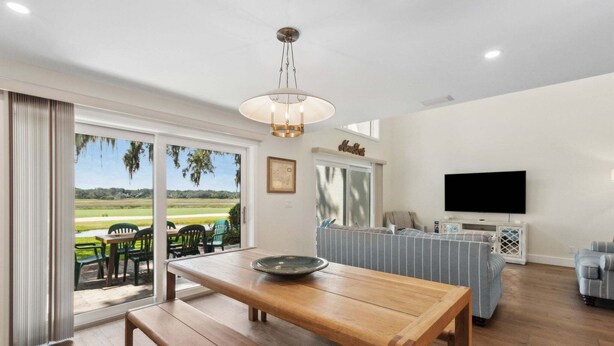 A spacious living room with a wooden dining table, a sofa set, a television, and a view of a golf course through large sliding glass doors. - Renovated, Stunning Marsh Views,  2BR condo on Amelia Island Plantation (Fernandina Beach)
