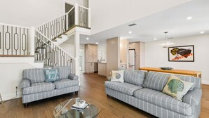A spacious living area with two grey-striped sofas, a glass coffee table, and a staircase with a modern railing. - Renovated, Stunning Marsh Views,  2BR condo on Amelia Island Plantation (Fernandina Beach)