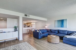 A modern living room with a sectional sofa, a dining area, and a kitchen in the background.