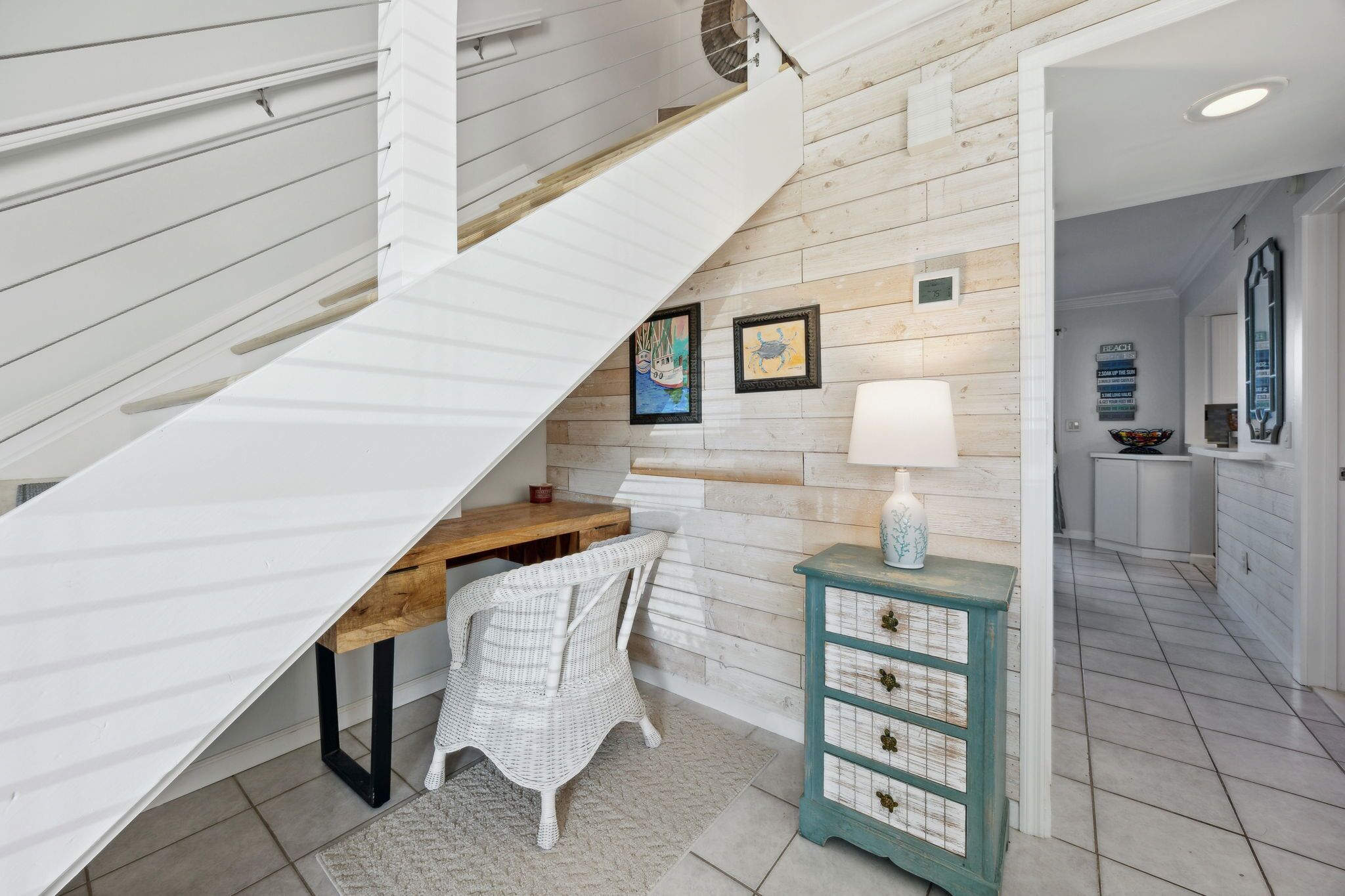 Een trap met een witte leuning leidt naar een plateau. Daaronder staat een houten bureau met een stoel, een kleine tafel en een decoratieve lamp.