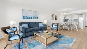 Un salon moderne comprenant un canapé, deux fauteuils, une table basse en verre et un coin repas avec une table et des chaises blanches.