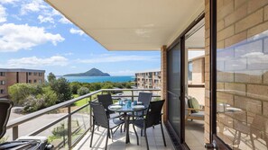 A balcony with a table, chairs, and a view of the sea and a mountain. - 'Shoaley Shores on Intrepid'  Overlooking Shoal Bay Beach (Nelson Bay)