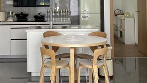 Una cocina moderna con armarios blancos, una isla central con una mesa redonda y cuatro sillas, una lámpara colgante y un refrigerador.