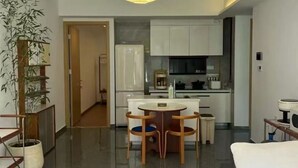 Una habitación de hotel moderna con una cama grande, una zona de comedor con una mesa redonda y sillas, una cocina y una planta grande en maceta.
