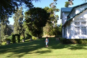 A child walking on a well-maintained lawn towards a white building with a blue roof. - Brockenhurst Bungalow (Nuwara Eliya)