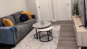Un salon moderne avec un canapé gris, une petite table ronde et un téléviseur posé sur un meuble en bois.