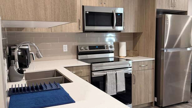 Une cuisine moderne avec des meubles en bois, des appareils en acier inoxydable et une serviette bleue posée sur le plan de travail.