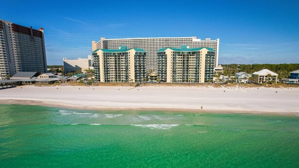 Un hotel fronte spiaggia con diversi edifici a grattacielo, una spiaggia sabbiosa e acque turchesi cristalline.