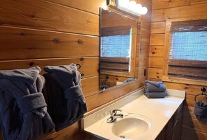 A wooden cabin bathroom with a sink, mirror, and towels. - Hanky Panky: Pet Friendly, Creek, Close to Downtown Pigeon Forge (Pigeon Forge)