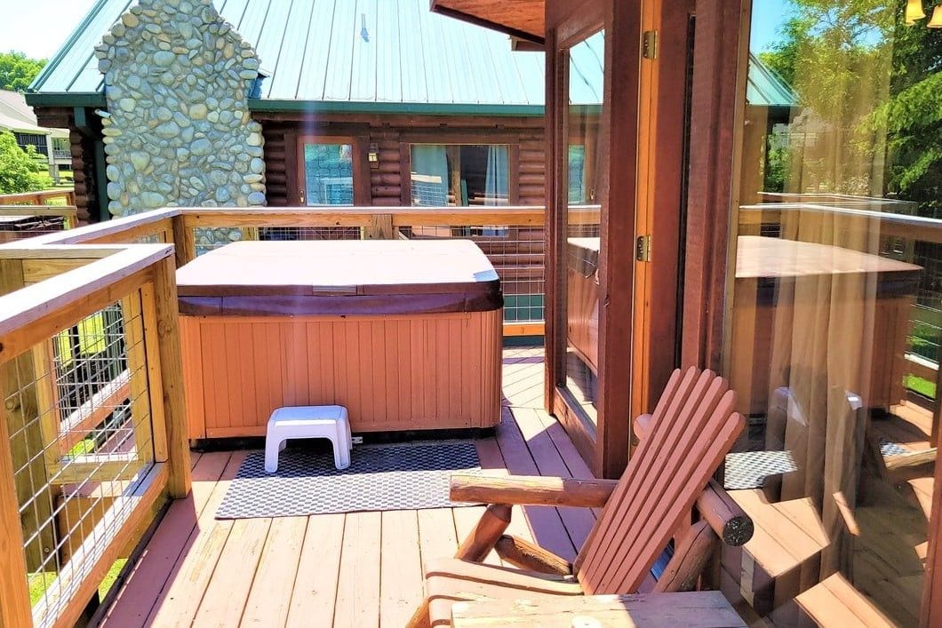 A wooden deck with a hot tub, a wooden chair, and a small stool.