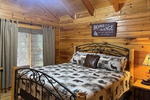 A cozy wooden cabin room with a bed featuring a quilt with animal prints, a sign on the wall that reads "HOME ON THE RANGE," and a window with curtains. - Hanky Panky: Pet Friendly, Creek, Close to Downtown Pigeon Forge (Pigeon Forge)