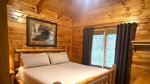A wooden cabin room with a bed, a framed picture on the wall, and a window with curtains. - Skinny Dippin: Free Tickets, Pet Friendly, Creek (Pigeon Forge)