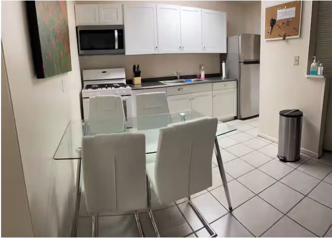 A modern kitchen with white cabinets, a glass table, and two white chairs.