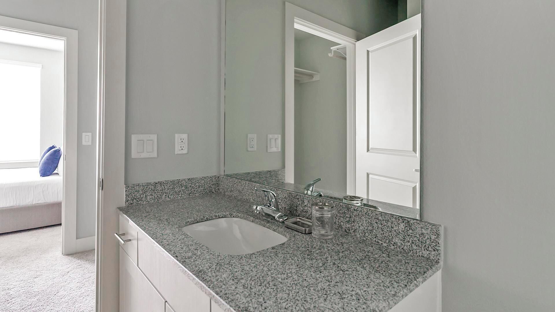 Une salle de bain avec un lavabo doté d’un plan de travail en granit, un miroir et une porte blanche.