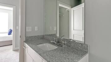 Une salle de bain avec un lavabo doté d’un plan de travail en granit, un miroir et une porte blanche.