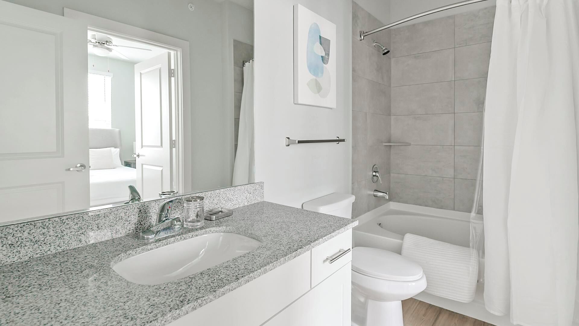 Un baño moderno con lavamanos de granito, inodoro blanco y ducha a ras de suelo con puerta de vidrio.