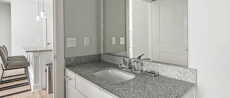 Een moderne badkamer met een granieten aanrechtblad, een wastafel en een spiegel.