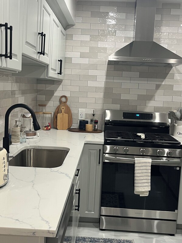 Una cocina moderna con azulejos tipo metro blancos, electrodomésticos de acero inoxidable y una campana extractora negra.