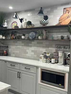 Una cocina con armarios blancos, microondas, cafetera y varios objetos decorativos en estantes.