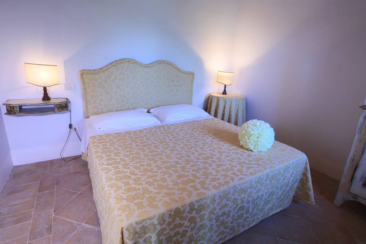 A neatly made bed with a patterned bedspread, two bedside lamps, and a small table with a book on each side.
