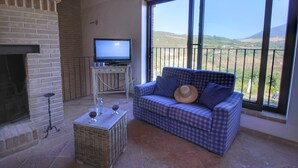 A cozy living area with a checkered sofa, a television, a fireplace, and a balcony with a scenic view. - Holiday Home With Pool Near Assisi (Assisi)