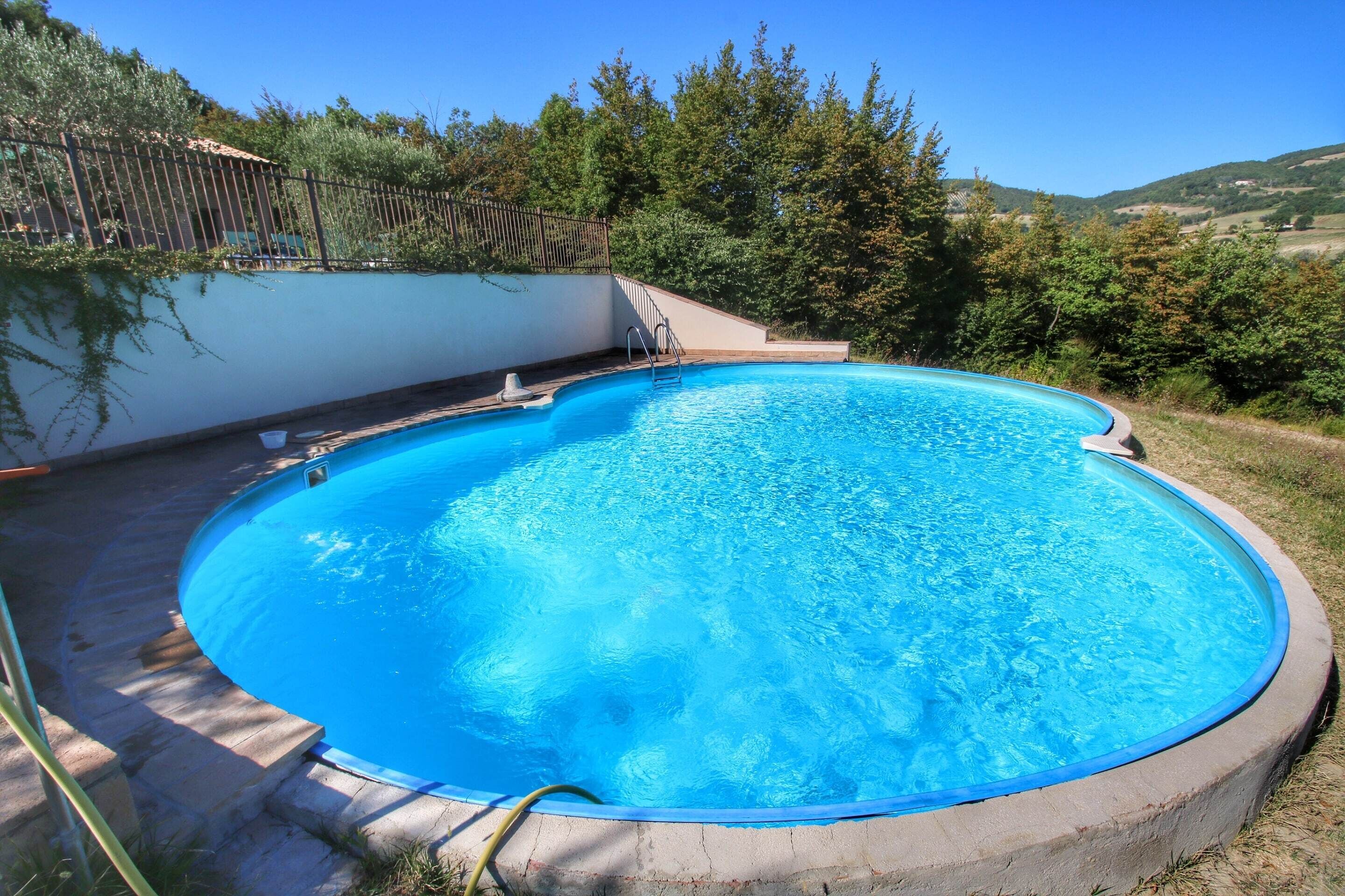 Una piscina circolare con bordo in cemento, circondata da un prato e alberi.