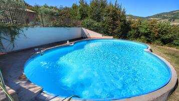 Una piscina circolare con bordo in cemento, circondata da un prato e alberi.