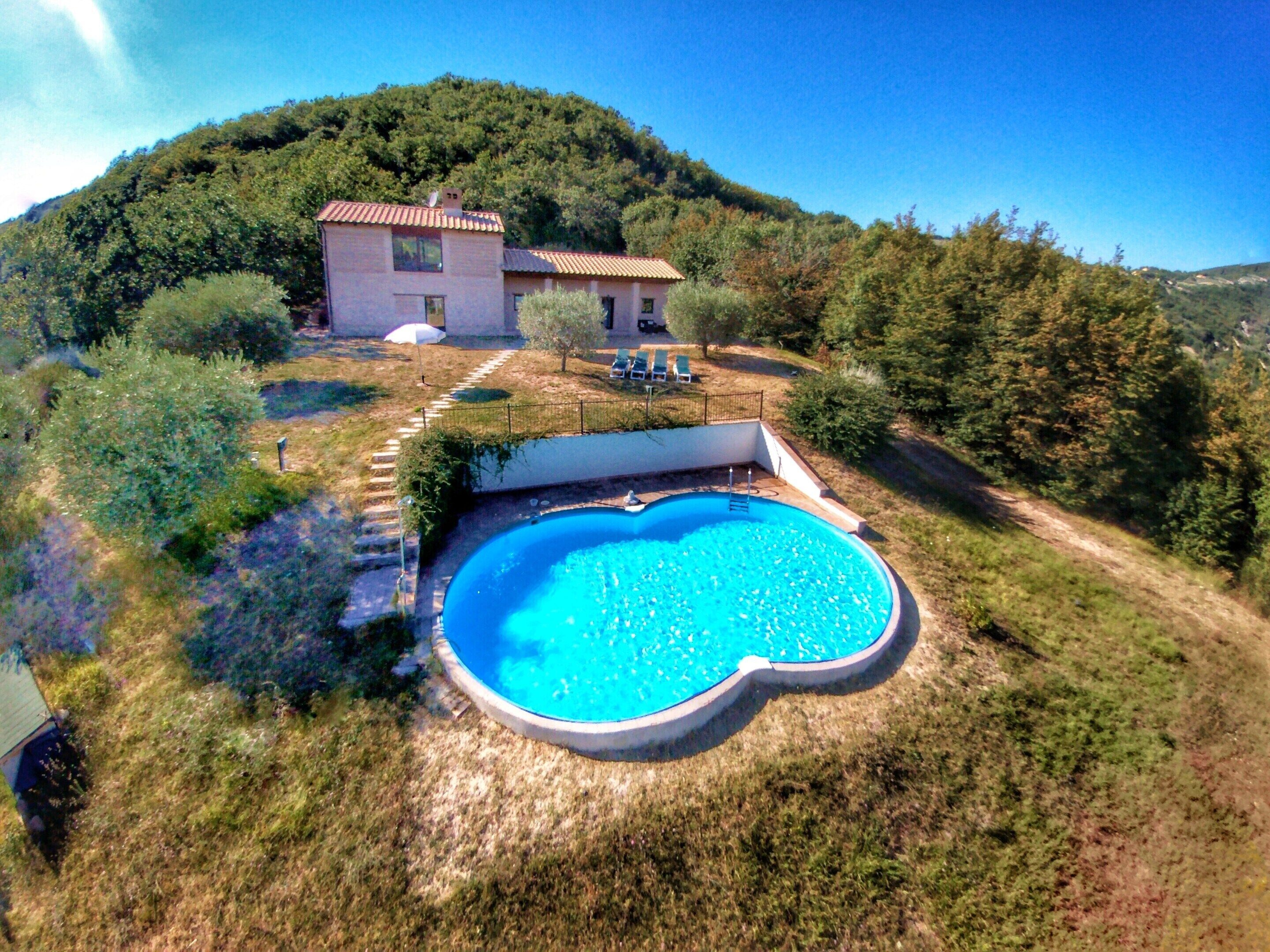 Una casa con piscina circondata da un giardino e una collina sullo sfondo.