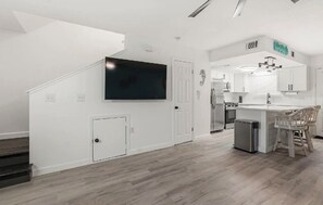 A modern kitchen with white cabinetry, a large TV, and a bar area with stools. - Very clean modern style all new remodel with pools and lots of amenities! PCB (Panama City Beach)