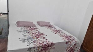 Une petite chambre avec un lit simple, une couvre-lit à motifs floraux et deux oreillers.