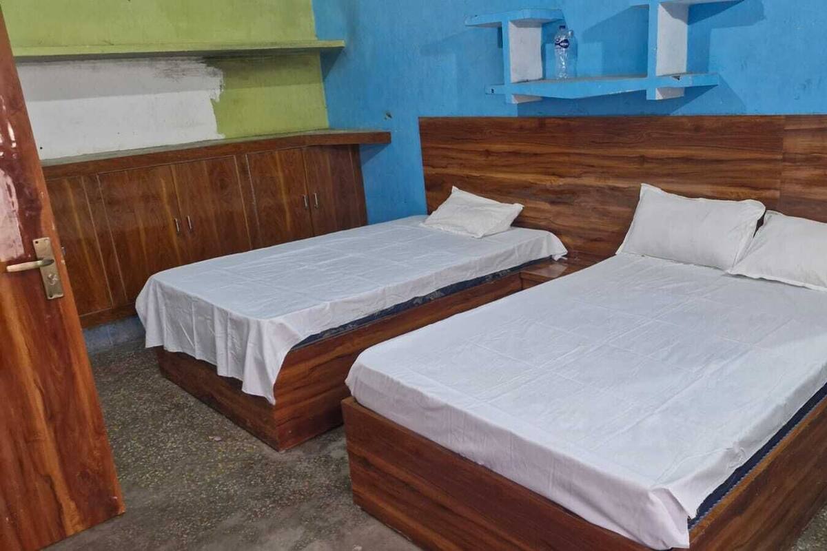 Una habitación con dos camas de madera, cada una con ropa blanca. Hay un armario de madera y un estante con una botella de agua.