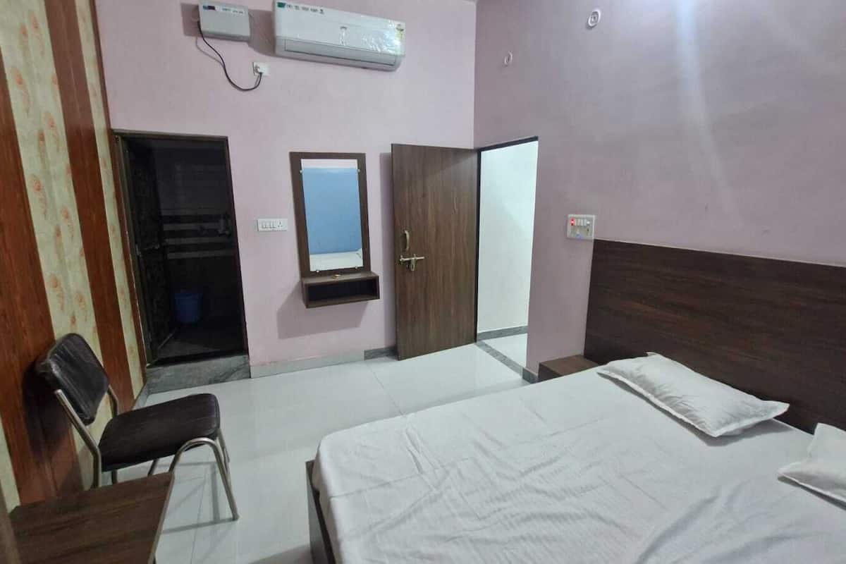 Habitación de hotel con cama, escritorio, silla, armario, espejo y aire acondicionado.