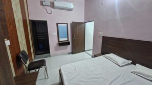 A hotel room with a bed, a desk, a chair, a wardrobe, a mirror, and an air conditioning unit. - Hanumant Kripa Paying Guest House (Faizabad)