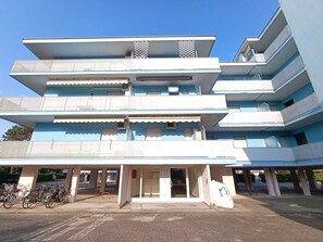 Un edificio de varios pisos con balcones, una entrada cubierta y bicicletas estacionadas afuera.
